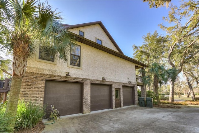 view of side of property with brick siding, stucco siding, driveway, and an attached garage