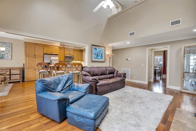 living area with light wood-style floors, visible vents, and ornamental molding