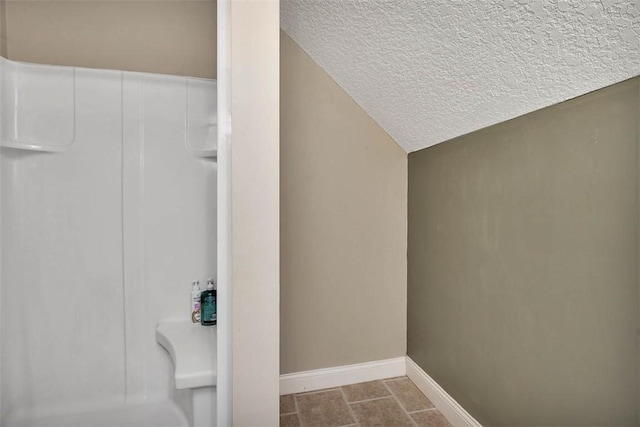 bathroom with a textured ceiling, vaulted ceiling, and baseboards