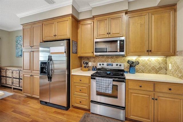 kitchen featuring light wood finished floors, ornamental molding, stainless steel appliances, and light countertops