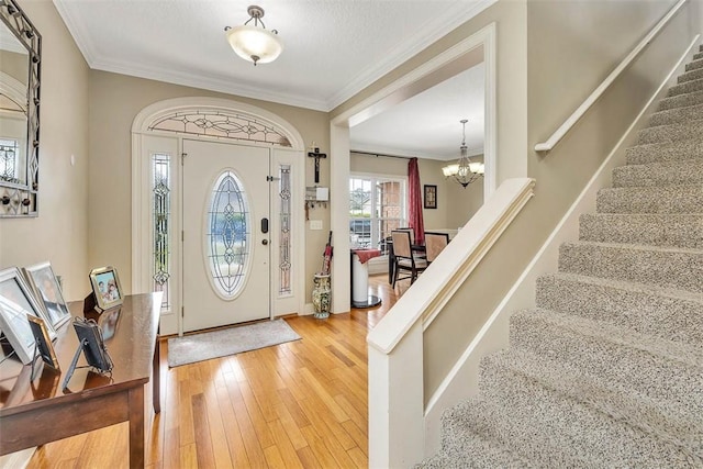 foyer featuring a textured ceiling, light wood-style flooring, a notable chandelier, stairs, and ornamental molding