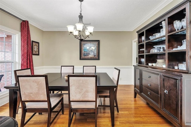 dining room with a wainscoted wall, crown molding, a chandelier, and light wood-style floors