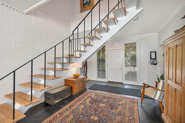 entryway with stairway, brick wall, crown molding, and a towering ceiling