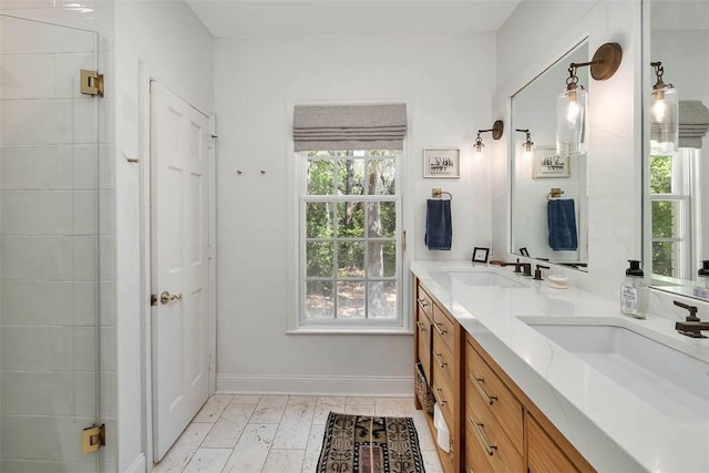 bathroom with double vanity, baseboards, a shower with door, and a sink