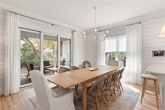 dining space with an inviting chandelier, ornamental molding, wood walls, and light wood-type flooring