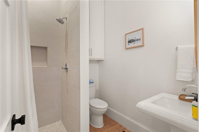 bathroom featuring hardwood / wood-style flooring, toilet, sink, and a tile shower