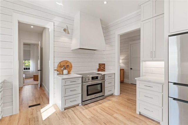 kitchen featuring white cabinetry, appliances with stainless steel finishes, light wood-type flooring, and wall chimney range hood