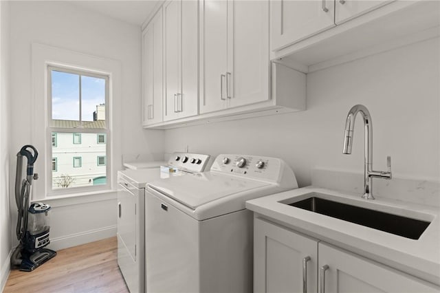 laundry area with cabinets, sink, washer and clothes dryer, and light hardwood / wood-style floors