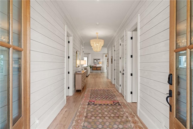 corridor with wood walls, ornamental molding, a notable chandelier, and light hardwood / wood-style flooring