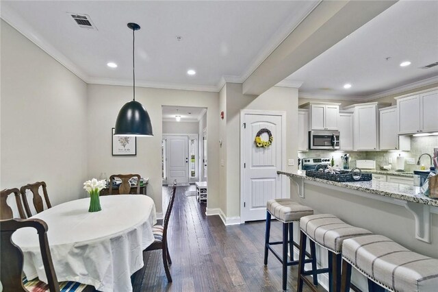 dining space with sink, dark wood-type flooring, and ornamental molding