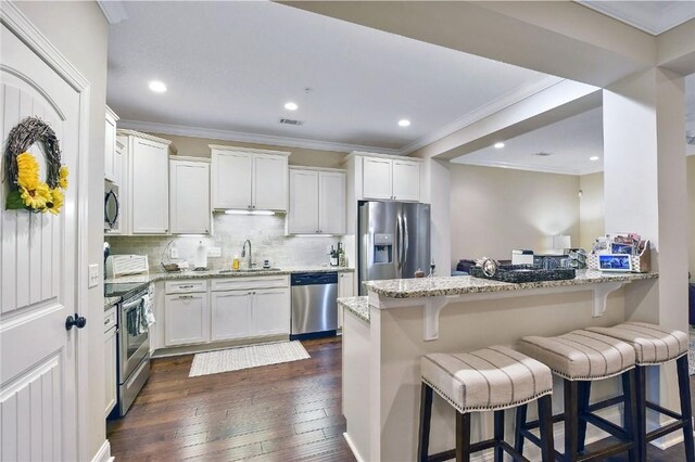 kitchen featuring white cabinets, dark hardwood / wood-style floors, light stone countertops, appliances with stainless steel finishes, and kitchen peninsula