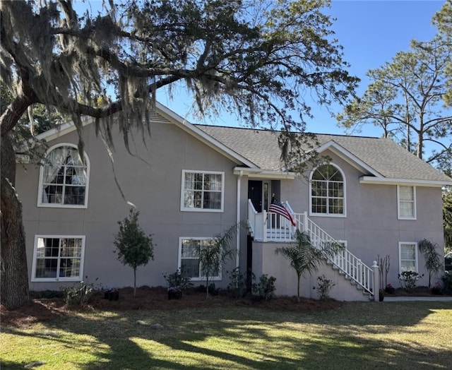 view of front of property featuring stucco siding, a front yard, and roof with shingles