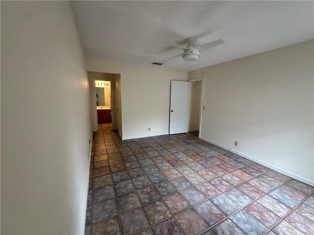 unfurnished bedroom featuring stone finish floor, a ceiling fan, baseboards, ensuite bathroom, and visible vents