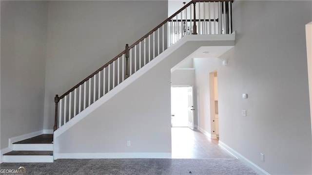 staircase featuring carpet floors, baseboards, and a towering ceiling