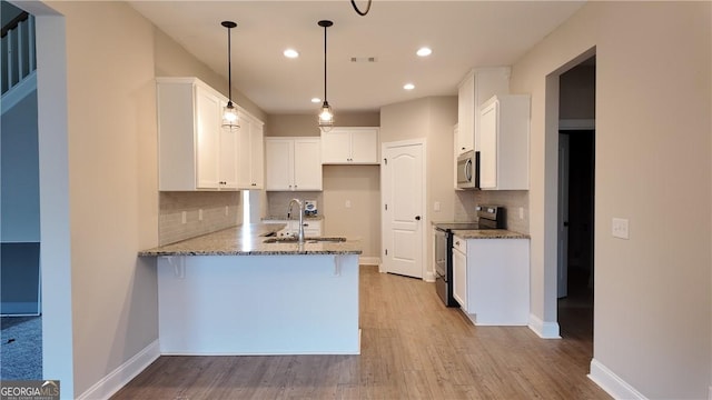 kitchen with a sink, a peninsula, stainless steel appliances, backsplash, and stone countertops