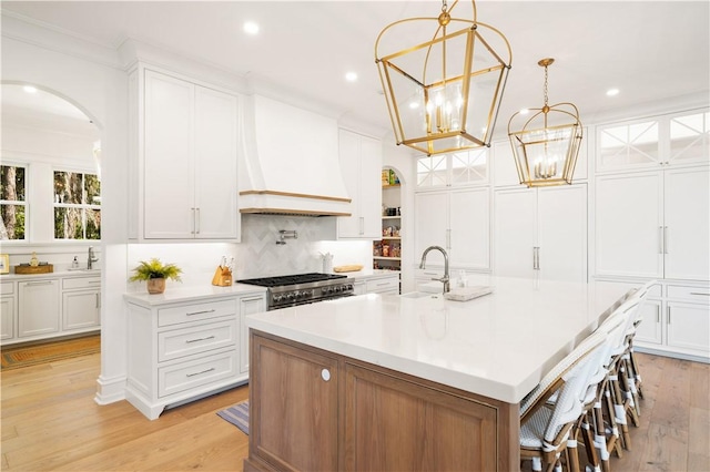 329 Saint Annies Ln, Saint Simons Island, GA 31522 - kitchen with arched walkways, light countertops, a chandelier, a kitchen island with sink, and white cabinets