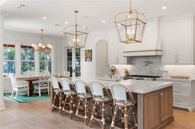 329 Saint Annies Ln, Saint Simons Island, GA 31522 - kitchen featuring a chandelier, backsplash, light wood-style flooring, a spacious island, and arched walkways