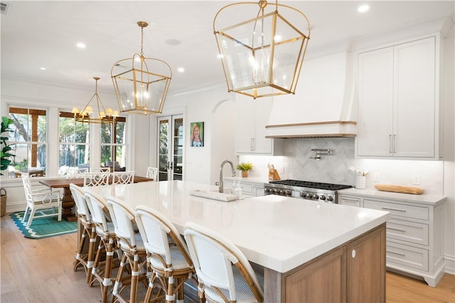 329 Saint Annies Ln, Saint Simons Island, GA 31522 - kitchen with a chandelier, backsplash, a center island with sink, light wood-style floors, and light countertops