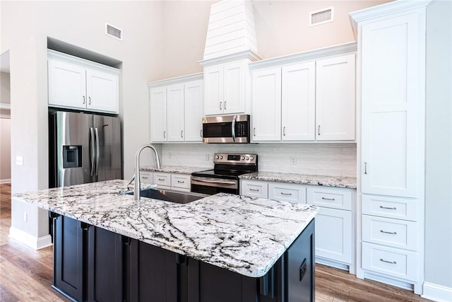 119 Silver Bluff Dr, Brunswick, GA 31523 - kitchen featuring appliances with stainless steel finishes, light wood-style floors, tasteful backsplash, white cabinets, and a kitchen island with sink