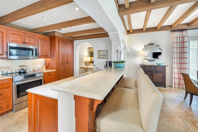 kitchen featuring a kitchen bar, sink, beamed ceiling, and appliances with stainless steel finishes