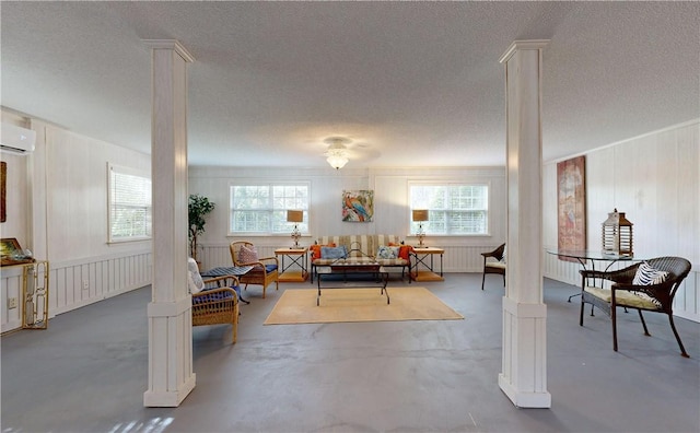 interior space with concrete flooring, a textured ceiling, a wall mounted air conditioner, and decorative columns