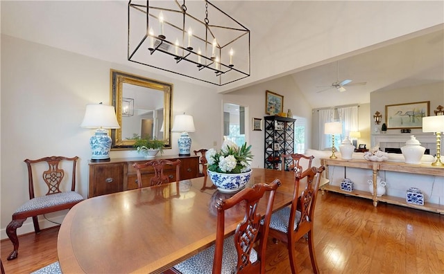 dining area with hardwood / wood-style floors, ceiling fan with notable chandelier, and vaulted ceiling