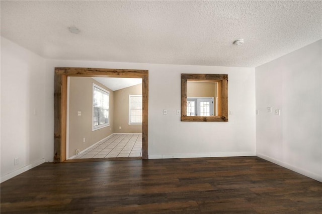 unfurnished room featuring dark hardwood / wood-style flooring, vaulted ceiling, and a textured ceiling