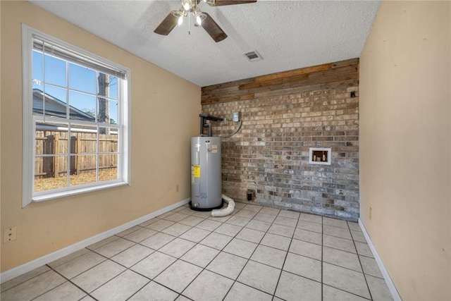 tiled empty room featuring water heater, ceiling fan, brick wall, and a textured ceiling