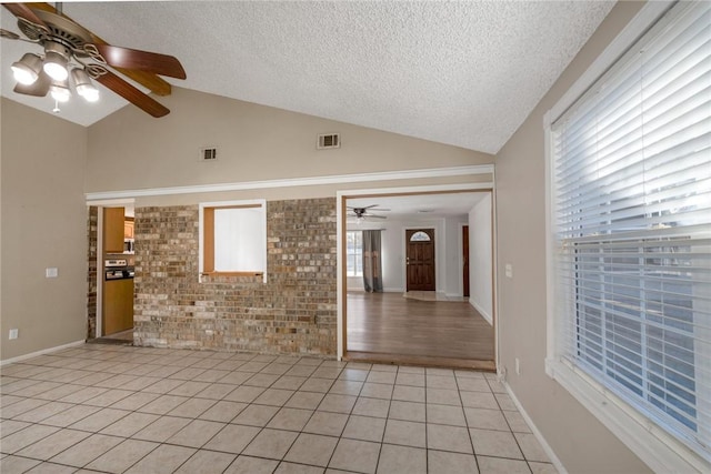 tiled empty room with a wealth of natural light, vaulted ceiling, a textured ceiling, and brick wall