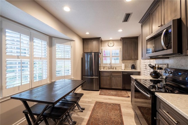 kitchen featuring dark brown cabinetry, sink, tasteful backsplash, light hardwood / wood-style flooring, and black appliances