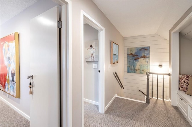 hallway with light carpet, vaulted ceiling, and wood walls