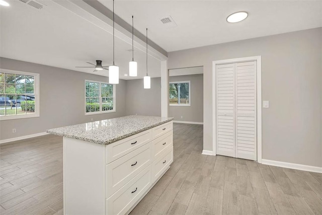 kitchen with light stone countertops, white cabinets, decorative light fixtures, and light wood-type flooring