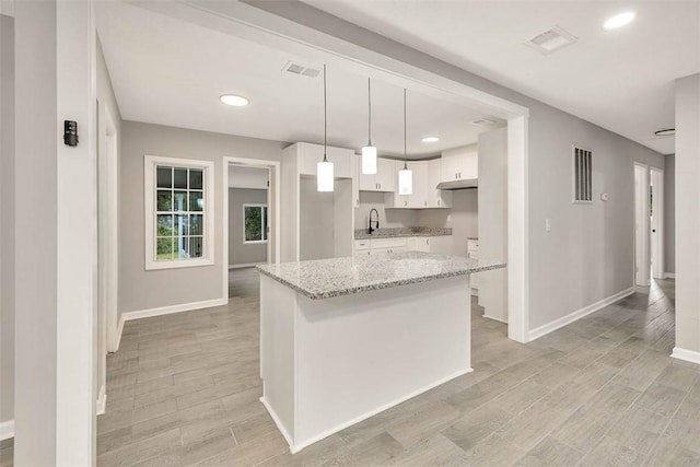 kitchen featuring sink, hanging light fixtures, light stone countertops, light wood-type flooring, and white cabinetry