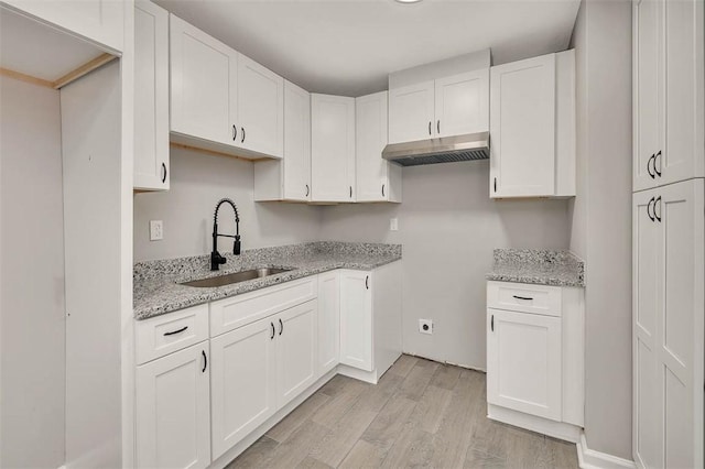 kitchen with light stone countertops, sink, white cabinets, and light wood-type flooring