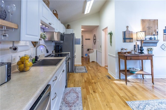 kitchen with stainless steel appliances, white cabinetry, sink, light wood-type flooring, and backsplash