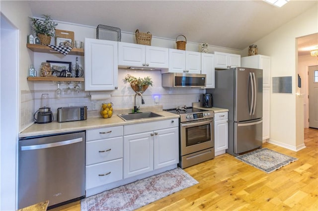 kitchen with sink, stainless steel appliances, white cabinets, and lofted ceiling