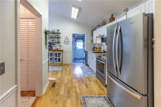 kitchen featuring appliances with stainless steel finishes, white cabinetry, sink, light hardwood / wood-style flooring, and vaulted ceiling