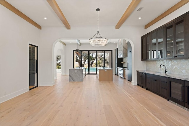 kitchen featuring tasteful backsplash, light stone counters, pendant lighting, light hardwood / wood-style floors, and dark brown cabinets