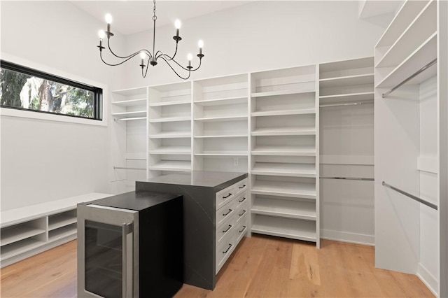 walk in closet with light hardwood / wood-style flooring, beverage cooler, and a notable chandelier