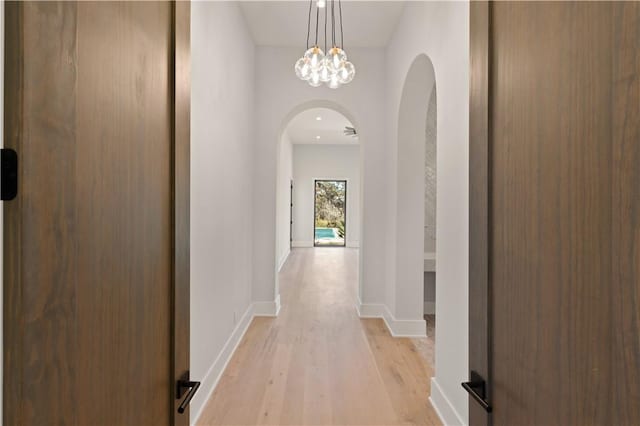 hall with light wood-type flooring and an inviting chandelier