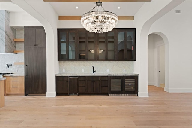 bar featuring dark brown cabinets, tasteful backsplash, and light hardwood / wood-style flooring