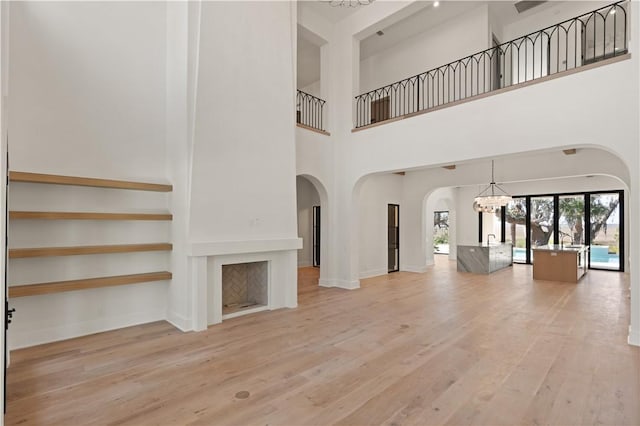 unfurnished living room with a notable chandelier, a large fireplace, light wood-type flooring, and a high ceiling