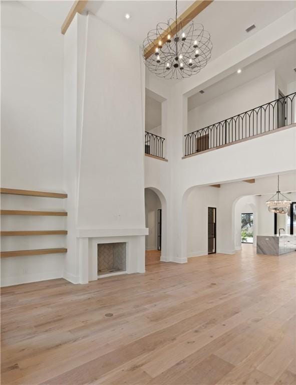 unfurnished living room featuring hardwood / wood-style flooring, a notable chandelier, a large fireplace, and a towering ceiling