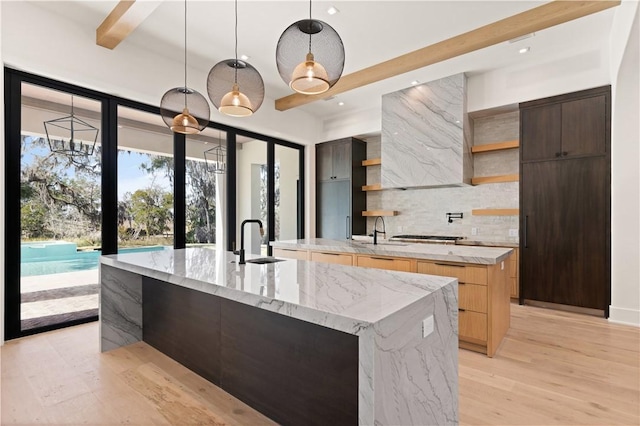 kitchen featuring sink, decorative backsplash, an island with sink, decorative light fixtures, and light stone counters