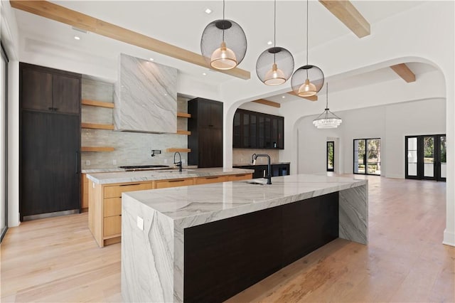 kitchen with beam ceiling, tasteful backsplash, light stone counters, pendant lighting, and a spacious island