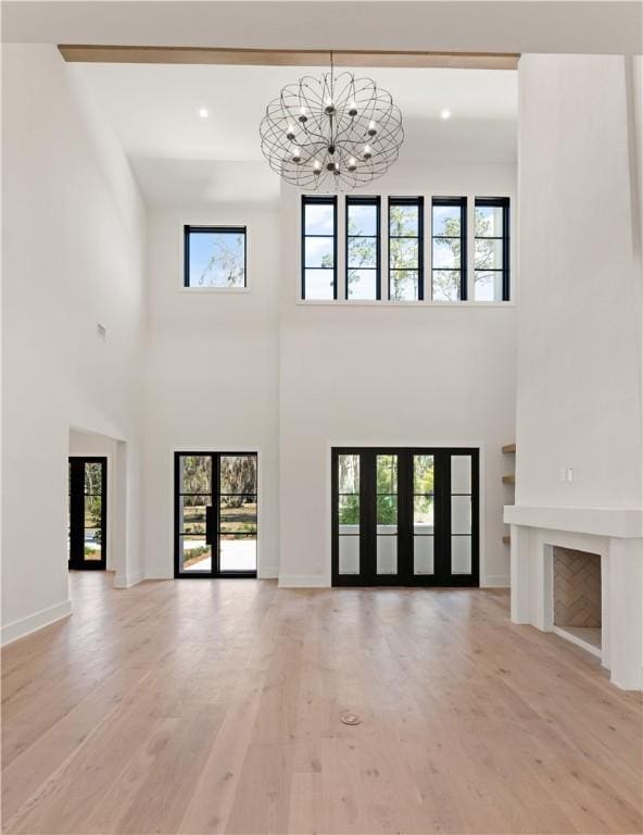 unfurnished living room featuring a towering ceiling, light hardwood / wood-style floors, an inviting chandelier, and plenty of natural light