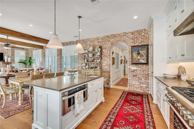 kitchen featuring beam ceiling, light wood-type flooring, white cabinetry, and brick wall