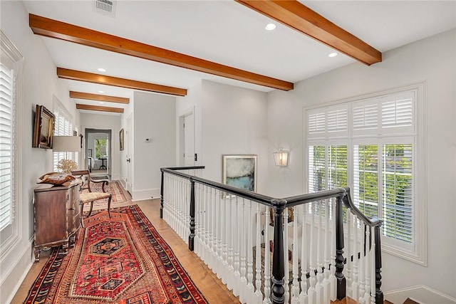 hall with beamed ceiling, wood-type flooring, and a wealth of natural light