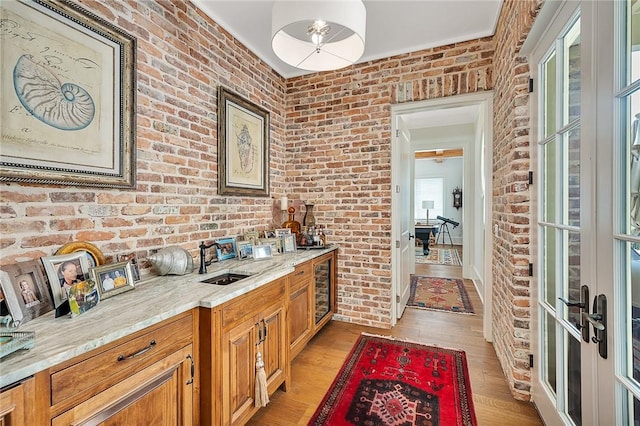 bar featuring sink, light stone counters, light hardwood / wood-style flooring, and brick wall