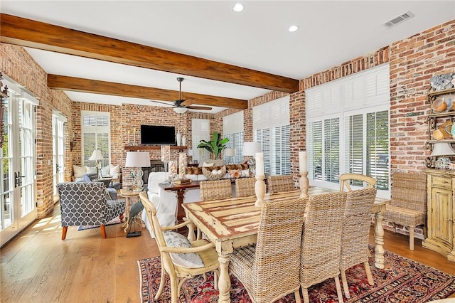 dining room featuring ceiling fan, light hardwood / wood-style floors, beam ceiling, and brick wall